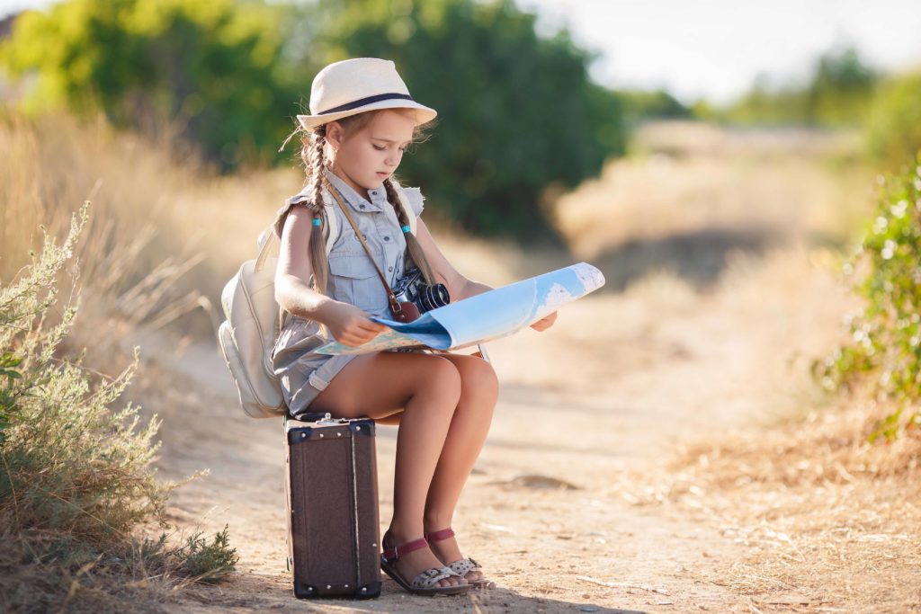 Child with vintage suitcase and city map on summer vacation. Travel and adventure concept. happy baby girl getting ready for the journey. Girl packs her bags and playing with binoculars.
